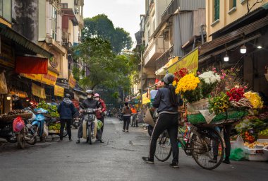 Bir çiçekçi yüklü bisikletini Hanoi, Vietnam 'daki Kau Go Eski Mahallesi' ndeki dükkanların önünden geçirir..