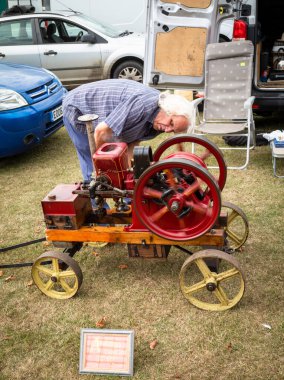 Adamın biri 1915 model Amanco Chore Boy sabit motorlu West Sussex, İngiltere 'deki Wisborough Green Village Fete' e doğru eğildi..