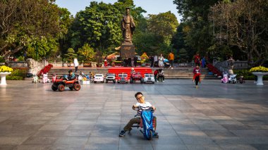Genç Vietnamlı bir çocuk, efsanevi imparator Ly Thai 'nin dev bronz heykelinin önünde üç tekerlekli bisiklete biniyor.