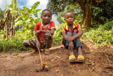 İki küçük kardeş, Tanzanya 'nın kırsalında Marumbo' da ev yapımı bir oyuncakla ağaçların yanında oturuyor..