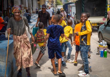 Orta Dar es Salaam, Tanzanya 'da bir grup okul üniformalı çocuğun yanından geçen yaşlı fakir bir kadın görülüyor.