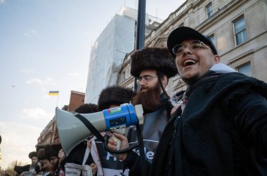 Londra / İngiltere - 9 Aralık 2023: Megafonlu Müslüman bir adam, İsrail 'in Gazze' ye düzenlediği saldırılara karşı düzenlenen bir protestoda Siyonist karşıtı Haredi Yahudi grubu Neturei Karta veya Şehrin Koruyucuları ile birlikte ayakta duruyor.