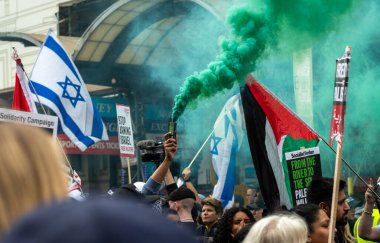 London, UK. 18 May 2024: A Pro-Palestinian protester holds a green flare as the Nakba 76 March for Palestine against Israeli attacks on Gaza passes hardline pro-Israel counter demonstrators at Piccadilly Circus in central London, UK.  clipart