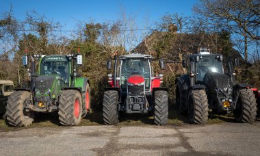 Üç büyük modern traktör, kıçlarını Wisborough Green, West Sussex, İngiltere 'de bir çite doğru kıvırdılar..