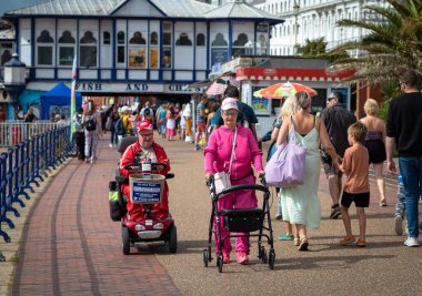 Engelli bir çift, Eastbourne İskelesi, Doğu Sussex, İngiltere 'nin yanındaki güvertede hareket halindeki bir scooter ve bir tekerlekli sandalye kullanıyor..