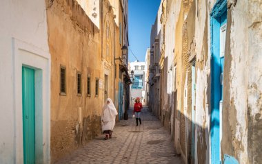 Geleneksel bir foutah giymiş yaşlı bir Tunuslu kadın ve Tunus 'un antik Medine' si Kairouan 'da genç bir kadın bir patikada yürüyor. Kairouan İslam 'ın dördüncü en kutsal şehridir ve UNESCO' nun Dünya Mirasları Alanıdır..