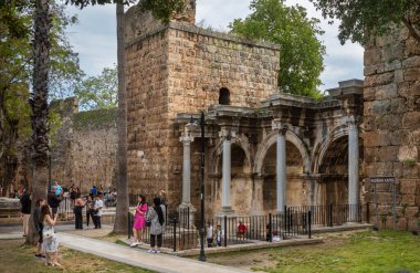 Turistler, Türkiye 'nin Kaleici kentindeki güzel korunmuş Roma dönemi Hadrian Kapısı' nı ziyaret ediyorlar (Türkiye)).
