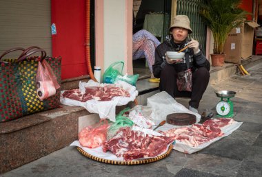 Bir kadın, orta Hanoi, Vietnam 'da kaldırımda domuz eti satarken erişte çorbası içiyor..