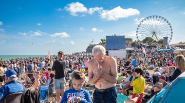 Genç bir çocuk Eastbourne, Doğu Sussex, İngiltere 'de kalabalık bir plajda oynarken bir adam sigarasını yakıyor..