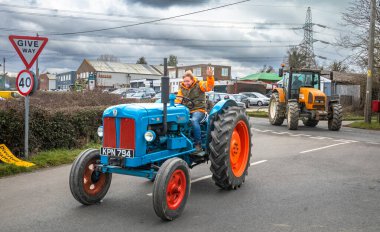 A participant in a charity tractor parade waves as he turns a corner in his vintage Fordson Major on a country lane in West Sussex, UK. clipart