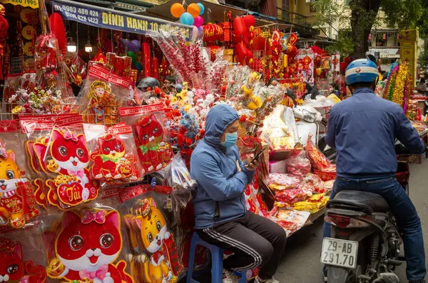 Tet için renkli kırmızı ve altın hediyeler satan Vietnamlı bir kadın tezgahtar Hang Ma, Hanoi, Vietnam 'da cep telefonuna bakar..