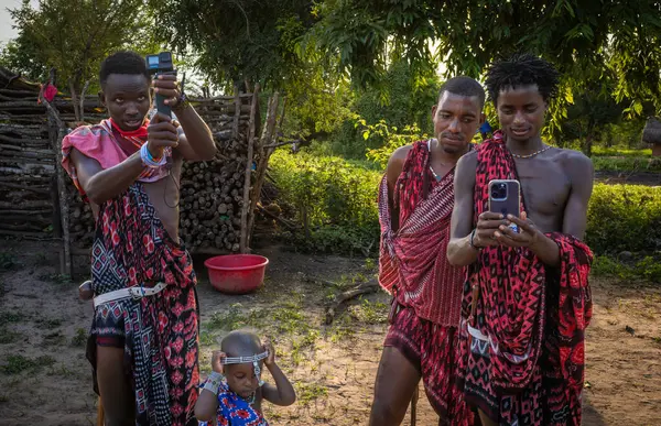 stock image Three young Maasai warrior tribesman look at a GoPro video camera and iPhone in Mikumi, Tanzania.