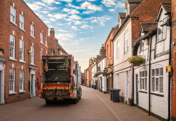 stock image A municipal refuse collection vehicle collects rubbish or trash from wheelie bins at sunrise in Dam Street, Lichfield, Staffordshire, UK.