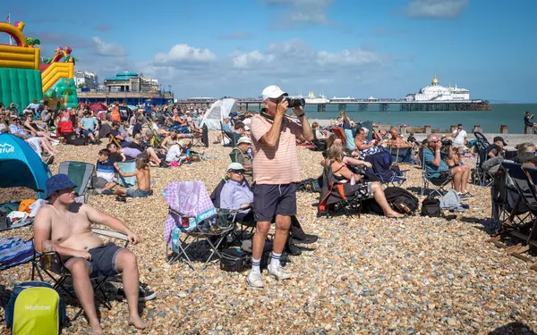 İnsanlar yazın sahilde fotoğraf çekmek ve Doğu Sussex, İngiltere 'deki Eastbourne İskelesi yakınlarında bir uçak gösterisi izlemek için toplanıyorlar..