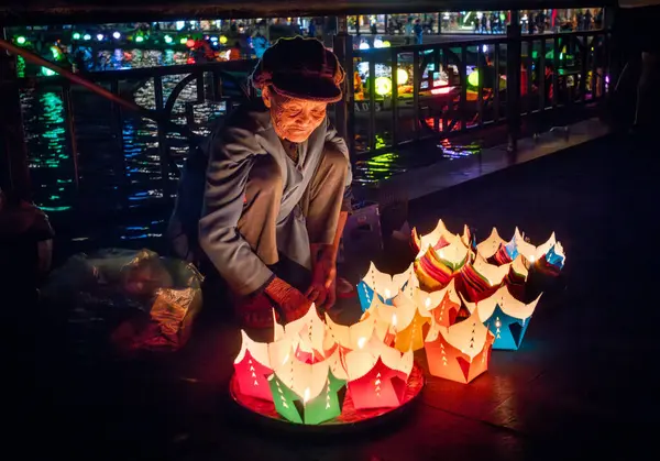 Yaşlı Vietnamlı bir kadın Hoi An, Vietnam 'da turistlere içinde mum bulunan yüzen fenerler satmak için köprüde oturuyor..