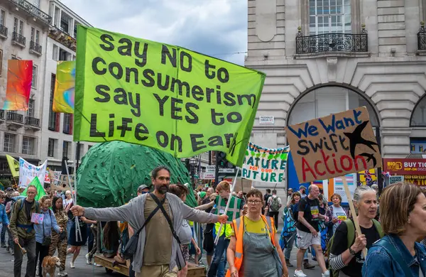 stock image London / UK - Jun 22 2024: A climate activist holds an anti-consumerism banner at the Restore Nature Now march for environmental protections. Organisations including the RSPB, WWF,  National Trust, Extinction Rebellion 