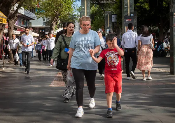 stock image In the bustling city of Antalya, Turkey, a young boy cries as his mother holds his hand and they walk through a crowded shopping street, as the late afternoon sun casts a warm glow over the cityscape. 