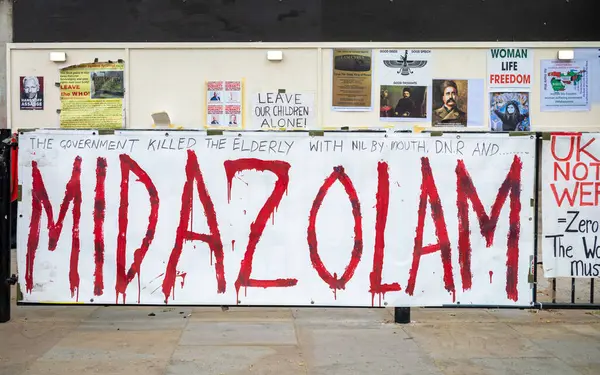 stock image A large banner at a protest camp in opposite Downing Street in Whitehall, London, highlights the drug Midazolam and accuses the government of hospital-related deaths. The protest also advocates leaving the World Health Organization. 