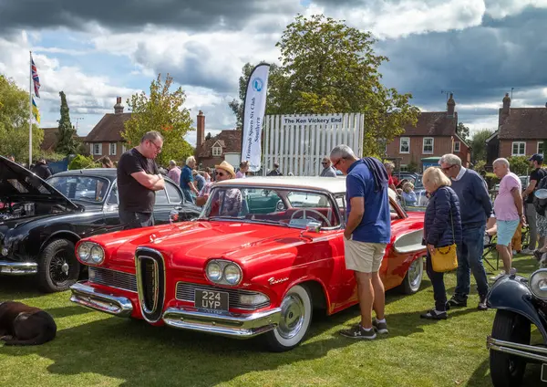 İnsanlar, Wisborough Green Village Fete, West Sussex, İngiltere 'den gelen parlak kırmızı 1958 Ford Edsel arabasına bakmak için duruyor.