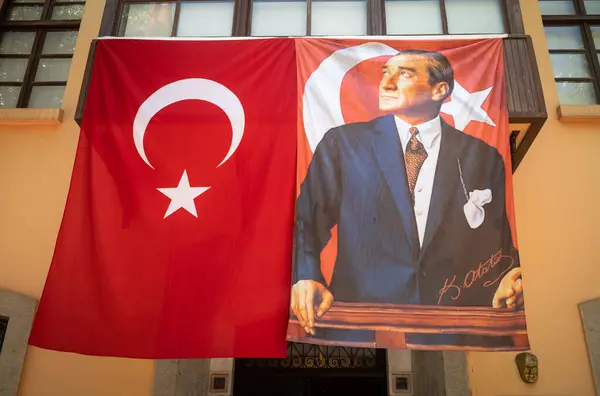 stock image A Turkish flag and an equal-sized banner featuring a portrait of Mustafa Kemal Ataturk above the entrance to a centre of Turkey's  patriotic history at the Ataturk House Museum in Antalya, Antalya Province, Turkiye.