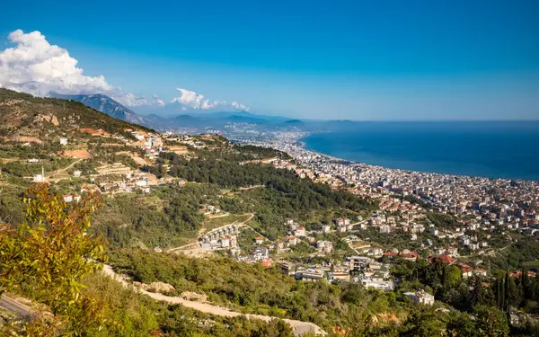 Türkiye 'nin (Türkiye) Alanya kentinin göz kamaştırıcı panoramik manzarası görkemli Taurus Dağları' nın eteklerinden (Toros Dağları) tepeden aşağıya, parlak Akdeniz kıyısına doğru süzülen tepeler, berrak, mavi bulutlu bulutların altında..