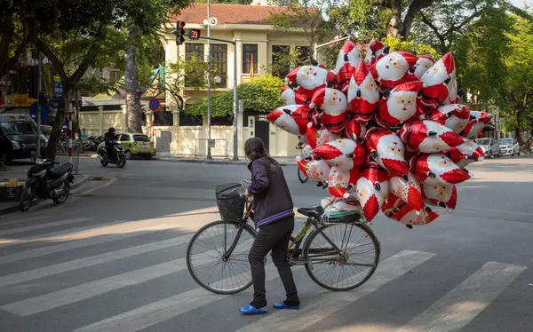 Bir sokak satıcısı, babasının Noel balonlarıyla dolu bisikletini Hanoi, Vietnam 'ın Fransız mahallesinde bir caddenin karşısına itiyor..