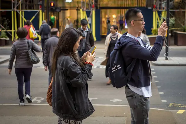 stock image A Chinese tourist couple stop to use their smartphones in Regent Street, London, UK.