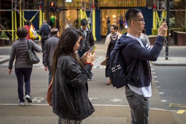 A Chinese tourist couple stop to use their smartphones in Regent Street, London, UK.