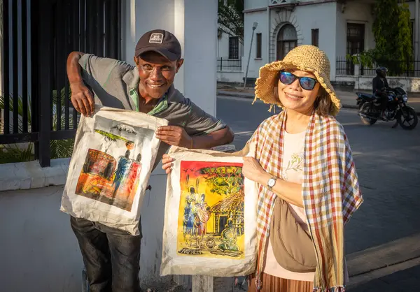 stock image A street hawker tries to sell his Maasai style paintings to a passing Asian female tourist in Dar es Salaam, Tanzania.