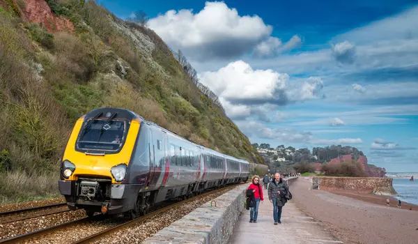 Bir tren Teignmouth, Devon, İngiltere 'de deniz kenarında yürüyen orta yaşlı bir çiftin yanından geçiyor..
