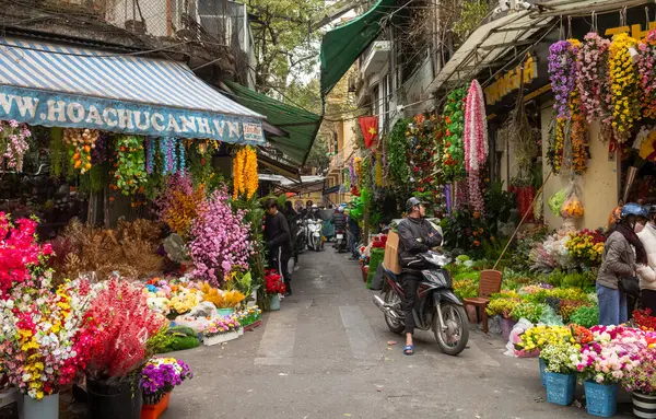 Motosikletli bir adam, Hanoi, Vietnam 'ın Eski Mahallesi' nde, bir ara sokağın iki yanındaki dükkanlarda suni renkli çiçekler satarak bekliyor..