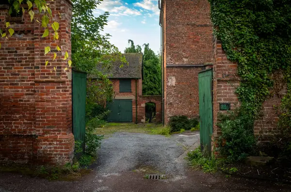 Lichfield, Staffordshire, İngiltere 'deki katedralin karşısındaki yeşil ahşap kapılardan görünen antik bir kırmızı tuğla ve yosun avlusu.