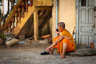 Kamboçya 'nın Phnom Penh kentindeki Saravoan Techo Pagoda avlusunda oturan turuncu cüppeli bir Budist keşiş cep telefonuyla sohbet ediyor..