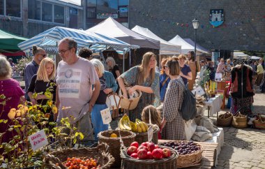İnsanlar Totnes, Devon, İngiltere 'nin merkezindeki geleneksel pazarda gıda ve giysi tezgahlarına göz atıyorlar..