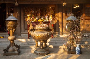 A large incense burner, or l hng, next to a shrine with offerings of fruit and cherry blossom inside Thuy Trung Tien Temple, or Cau Nhi, the ancient dog-worshipping temple on Truc Bach Lake, Hanoi, Vietnam.  clipart