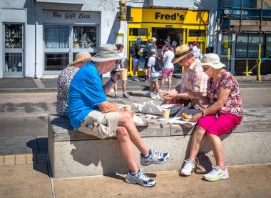 Emekli ve yaşlı iki çift yemek yemek için Batı Sussex, İngiltere 'deki Littlehampton rıhtımında balık ve patates kızartması yiyorlar..