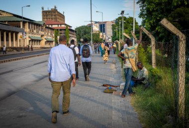 Banliyö sakinleri Kivokoni Yolu 'ndan Dar es Salaam, Tanzanya' daki Kigamboni Feribot Terminali 'ne doğru bir sokak satıcısını geçerek yürüyorlar.