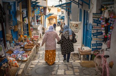 Türban takan iki Müslüman kadın, antik Medine, Susa, Tunus 'ta Rue El Aghalba' da bir hediyelik eşya dükkanının önünden el ele yürüyorlar. Medine UNESCO 'nun Dünya Mirası Bölgesi.