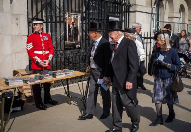 Silindir şapkalı iki yaşlı adam karılarıyla birlikte Londra 'da bir Coldstream Muhafız Ordusu çavuşunun önünden geçiyorlar.