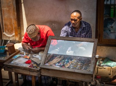 İki adam Tanzanya 'nın Zanzibar kentindeki Stone Town Market' te saat tamir ve satma tezgahında çalışıyor.