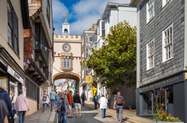 İnsanlar 14. yüzyılın doğu kapısı kemerinin yanında yürüyorlar. Büyük saati Totnes, Devon, İngiltere 'deki ana caddenin üzerinde duruyor..