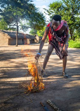 A Maasai warrior starts fire by friction after rubbing sticks together  in a village in Mikumi, Tanzania. clipart