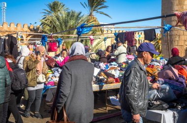 İnsanlar Sousse, Tunus 'taki Ribat ve antik Medine duvarlarının yanındaki geleneksel açık hava giyim pazarında alışveriş yapıyorlar..