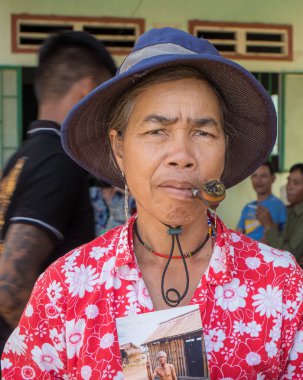 Brau etnik azınlığından orta yaşlı bir kadın, Kontum Vilayeti, Vietnam 'da, 30 yıl önce babasının elinde mızrak tutarken çekilmiş bir fotoğrafı olarak pipo içiyor.