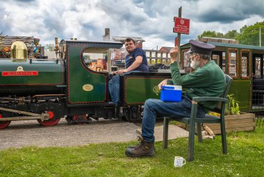 Bir gönüllü, South Downs Light Railway, Pulborough, İngiltere 'deki bir gardiyanın yanından demiryolu minyatür buharlı lokomotifini geçiyor.