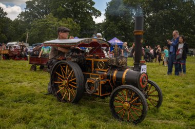 Storrington / UK - Jul 13 2024: A steam enthusiast drives his  scale model steam traction engine at Sussex Steam Fair, Parham, Storrington, UK. clipart