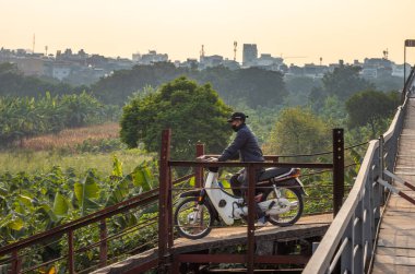 Motosikletli ve yüz maskesi takan bir motosikletli ve kasksız bir şekilde Long Bien Köprüsü 'nden Kızıl Nehir, Hanoi, Vietnam' daki bir adaya uçuyor..