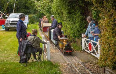 Ingfield Malikânesi, Five Oaks, West Sussex, İngiltere 'deki mini bir geçitten geçen yolcuları taşıyan minyatür dar bir buhar treni seyrediliyor..