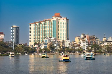 İnsanlar Truc Bach Gölü 'nde, Hanoi, Vietnam' daki Pan Pasifik Oteli 'nin yanındaki kuğu şekilli pedallı botlara biniyor.