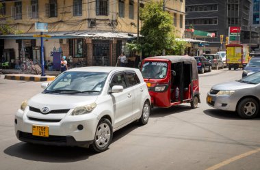 Orta Dar es Salaam, Tanzanya 'da bir caddede modern arabalar ve bir bajaji veya tuk sürüyor..